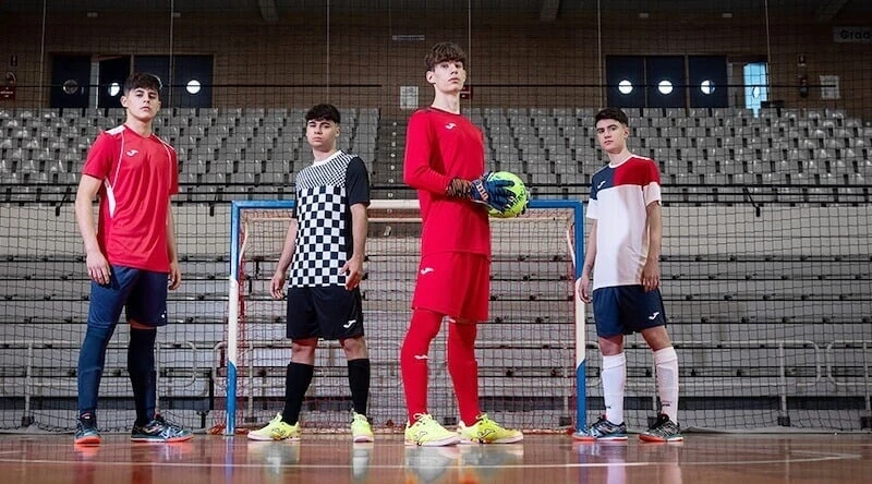 Tim futsal remaja memakai jersey Joma dengan desain berbeda berdiri di lapangan indoor 