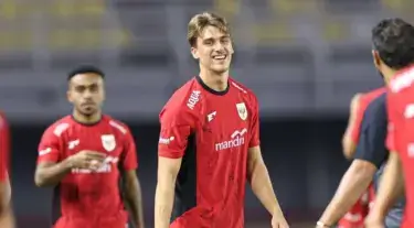 Pemain Timnas Indonesia berlatih mengenakan jersey merah hitam, tersenyum di tengah lapangan.