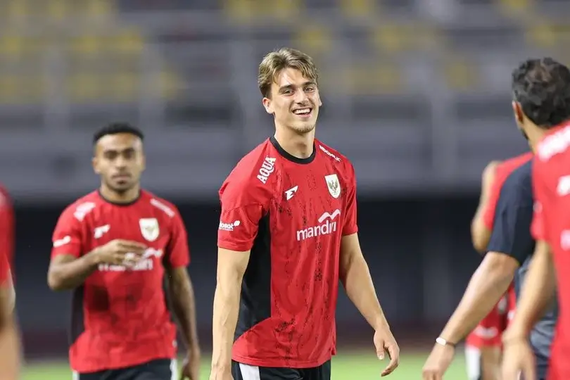 Pemain Timnas Indonesia berlatih mengenakan jersey merah hitam, tersenyum di tengah lapangan.