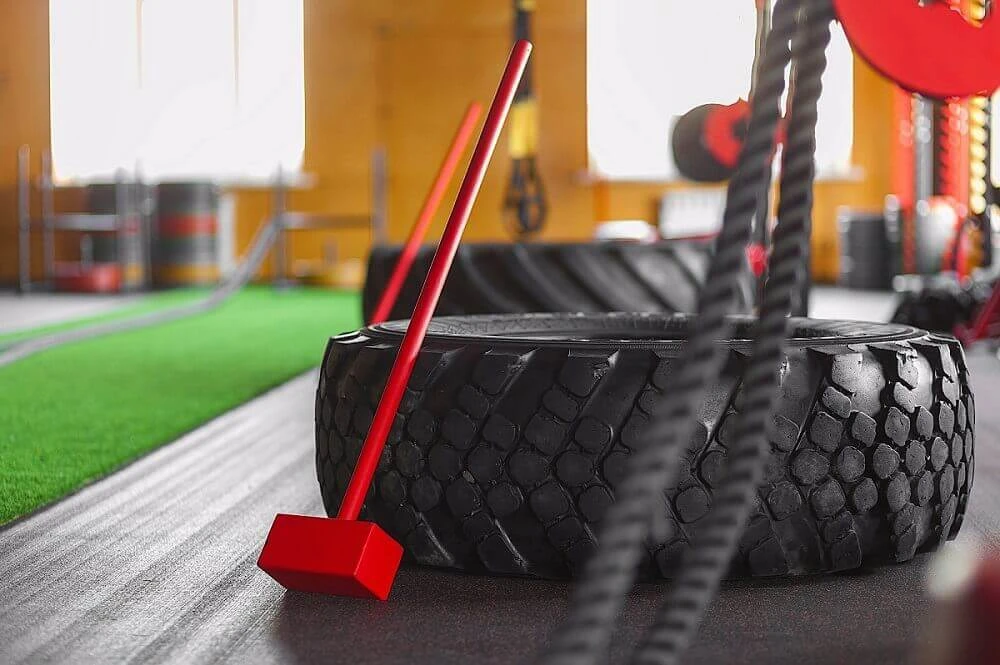 Palu godam merah bersandar pada ban truk besar di dalam area gym untuk latihan kekuatan
